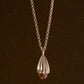 Gold necklace featuring a teardrop-shaped pendant with fluted ridges and a faceted amber-colored stone at the bottom, set against a dark brown background.